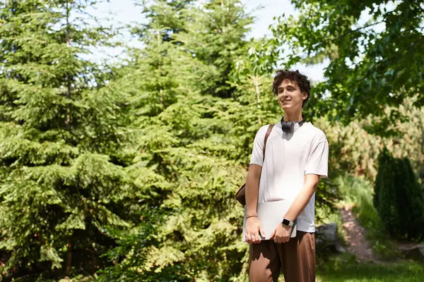 A young man with curly hair relaxes in a green park, soaking up the summer sunshine. — Stock Photo