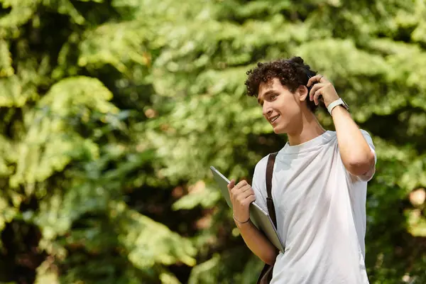 A young man with curly hair is casually spending time outdoors in a lush green park. — Stock Photo