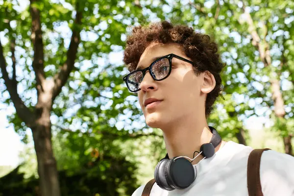 A young man with curly hair is relaxing in a vibrant summer park filled with greenery. — Stock Photo
