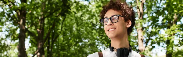 A young man with curly hair wearing a white t-shirt relaxes in a lush green park under the sun, banner — Stock Photo
