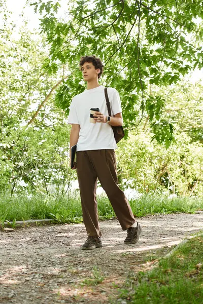 A young man enjoys a leisurely stroll through a lush summer park while checking his phone. — Stock Photo