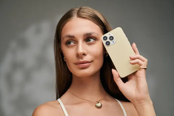 A beautiful young woman with tan skin is posing with smartphone in a studio setting. — Stock Photo