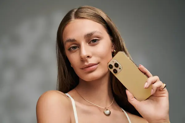 A young woman with tan skin and natural makeup poses confidently with her phone in a studio. — Stock Photo