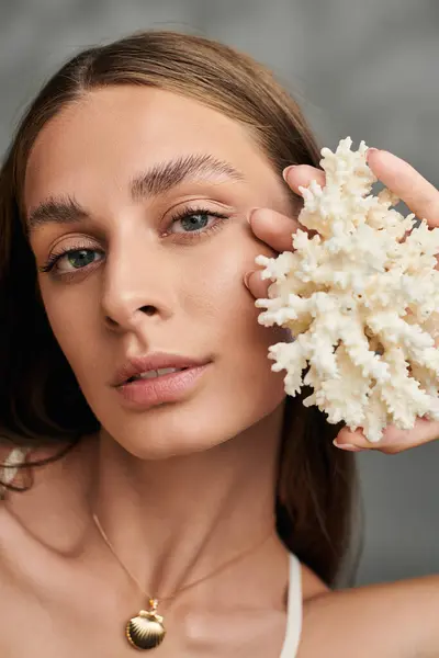 A pretty young woman showcases her natural makeup and summer glow, holding coral thoughtfully. — Stock Photo