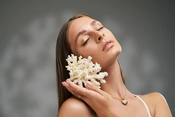 A pretty young woman with tan skin poses gracefully with coral in a studio, emphasising her natural beauty. — Stock Photo