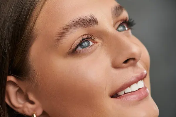 A radiant young woman with tan skin showcases her natural makeup against a grey background. — Stock Photo