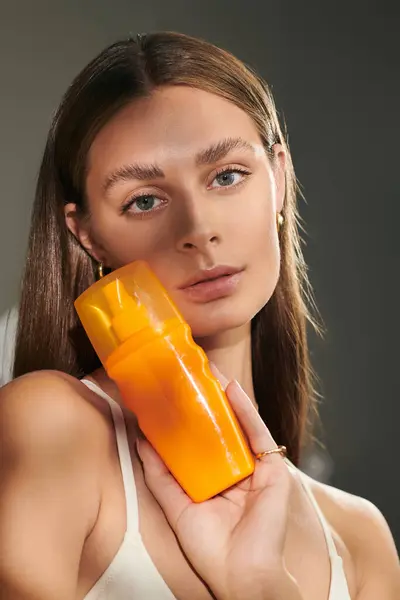 A young woman showcases her flawless tan skin and spf bottle in a summer studio setting. — Stock Photo