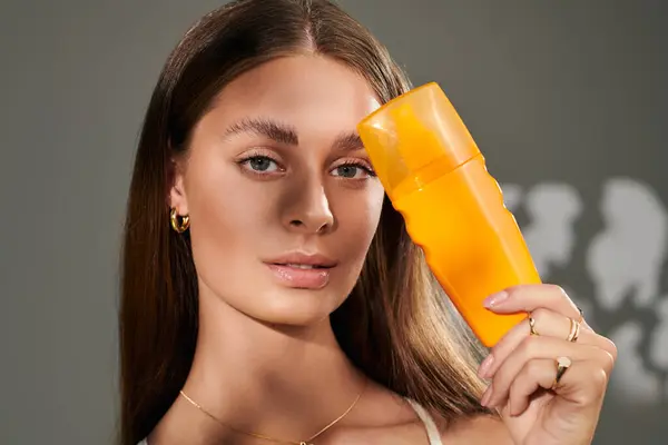 A pretty young woman showcases her natural makeup and tan skin while posing with sunscreen in a studio. — Stock Photo