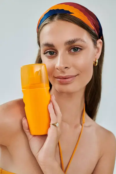 Young woman with tan skin poses confidently in a summer outfit while showcasing a bright sunscreen — Stock Photo