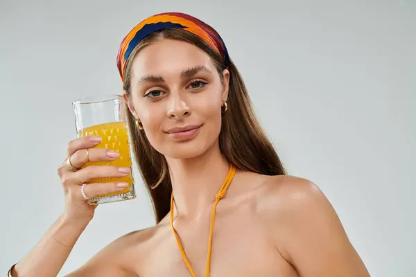 A pretty young woman with tan skin and a headscarf poses, holding a glass of juice in summer attire. — Stock Photo