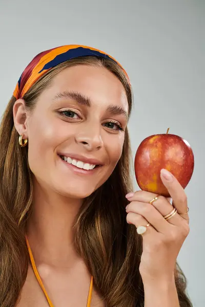 Bright and cheerful young woman celebrates summer with a fresh apple in a vibrant headscarf. — Stock Photo