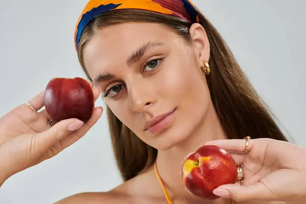 A young woman with tan skin poses in a summer outfit, holding fresh peaches in a studio. — Stock Photo