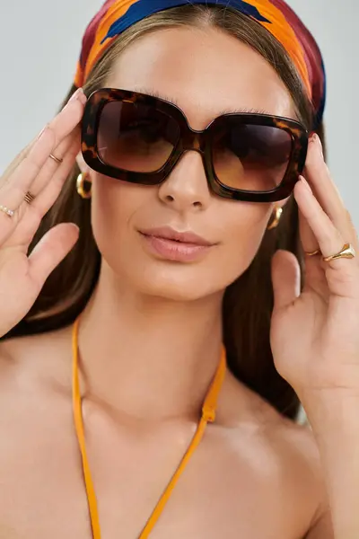 Chic young woman presents a stunning summer outfit complemented by a colorful headscarf in studio. — Stock Photo