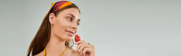 A young woman in a headscarf playfully poses with a strawberry, radiating summer elegance, banner — Stock Photo