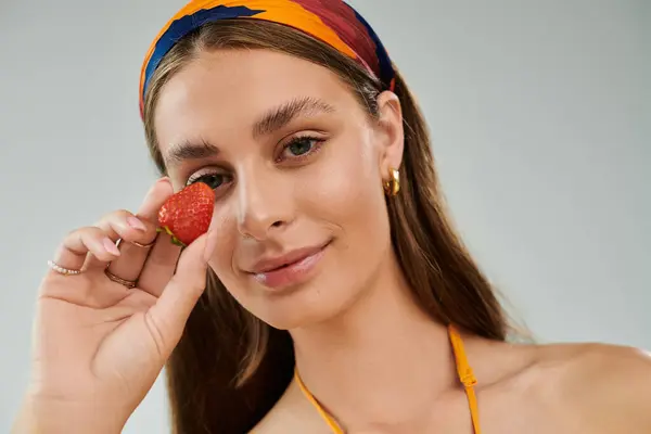 A pretty young woman holds a strawberry near her face, showcasing her summer fashion and beauty. — Stock Photo