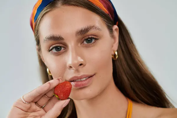 Young woman with tan skin showcases summer fashion while playfully holding a strawberry. — Stock Photo