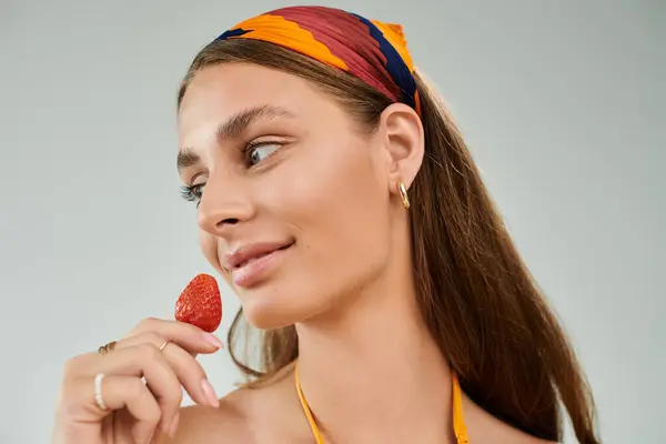 A woman with tan skin and a headscarf playfully poses with a strawberry, embodying summer. — Stock Photo