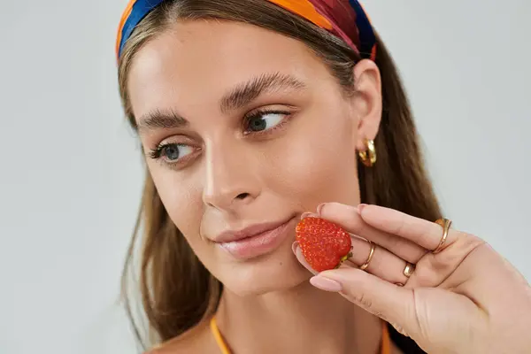 Young woman in a vibrant headscarf and natural makeup poses elegantly while holding a strawberry. — Stock Photo
