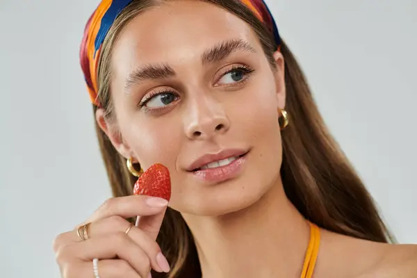A young woman with tan skin enjoys summer fashion while playfully holding a strawberry. — Stock Photo