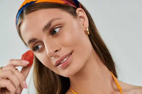 A young woman with tan skin showcases her summer style while playfully holding a strawberry. — Stock Photo