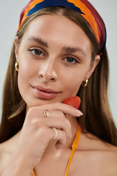 A pretty young woman poses with a strawberry, showcasing her summer outfit and natural beauty. — Stock Photo