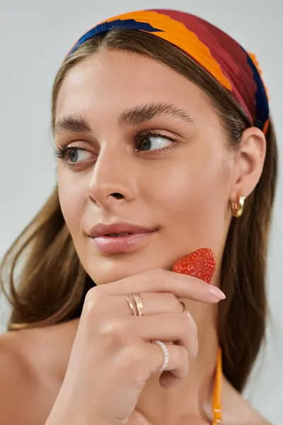 A young woman poses in a summer outfit, holding a strawberry and exuding beauty in a studio. — Stock Photo