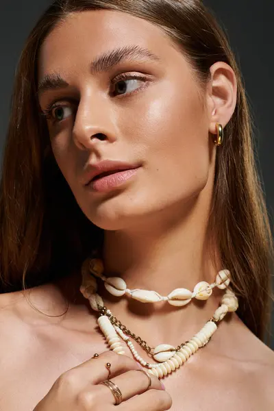 A beautiful young woman poses confidently, highlighting her summer seashell necklace. — Stock Photo