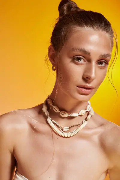 A confident young woman poses in a summer outfit and seashell necklace in a studio. — Stock Photo