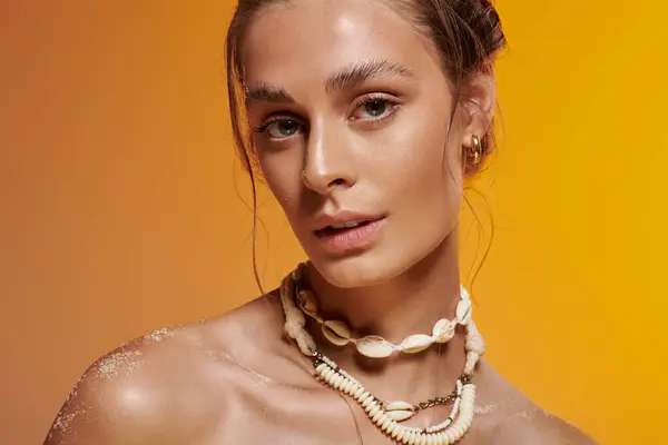 Young woman in a summer outfit poses confidently with a seashell necklace against a warm backdrop. — Stock Photo