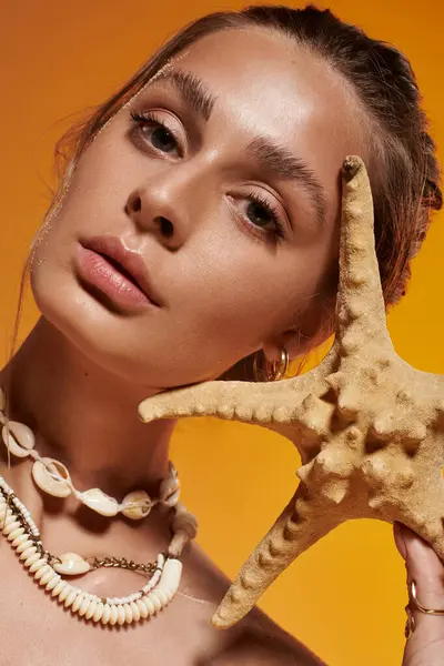 A beautiful young woman shows off a starfish and seashell necklace in a vibrant summer studio. — Stock Photo