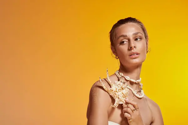 A stunning young woman showcases her summer style with a seashell necklace in a vibrant studio. — Stock Photo