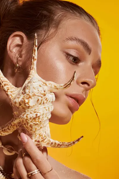 A young woman poses in a summer outfit, flaunting her seashell necklace against a bright backdrop. — Stock Photo