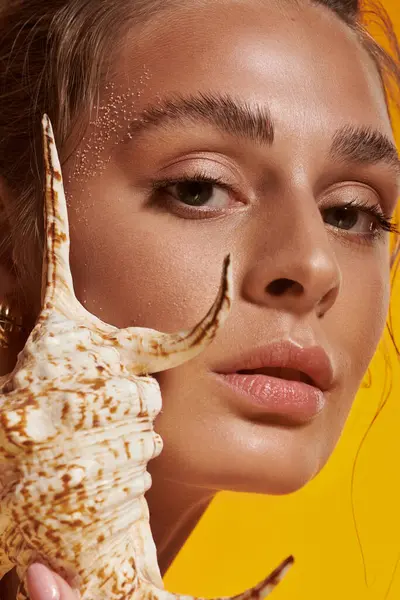 A beautiful young woman showcases her summer look with a seashell, exuding natural charm — Stock Photo