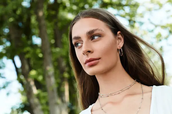 A young beautiful woman stands gracefully, basking in natural light surrounded by greenery. — Stock Photo