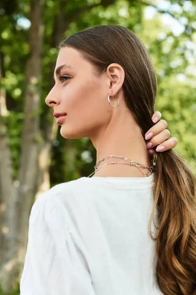 A young woman stands in a green park, gently brushing her hair and enjoying nature. — Stock Photo