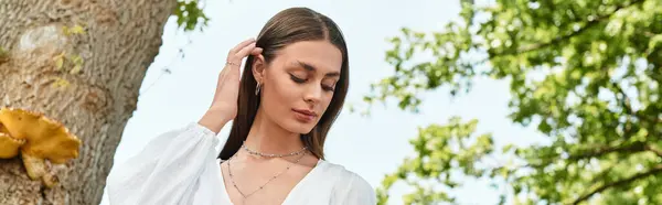 A young woman with long hair gracefully touches her neck, surrounded by lush greenery under the sun. — Stock Photo