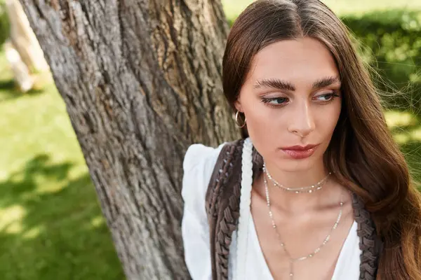 A young woman with long hair stands by a grand tree, deep in thought and savoring nature. — Stock Photo