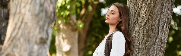 A young beautiful woman stands quietly by a tree, embracing nature and the warm sunlight. — Stock Photo