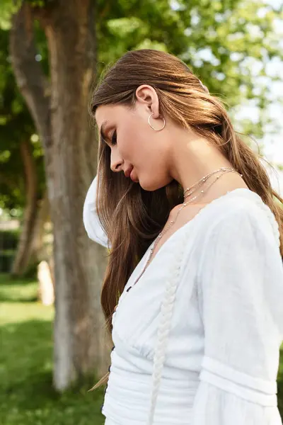 A young woman stands gracefully, lost in thought amidst vibrant greenery while dressed stylishly. — Stock Photo