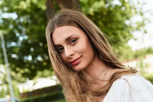 A young beautiful woman stands in a vibrant garden, exuding happiness and charm as she smiles. — Stock Photo