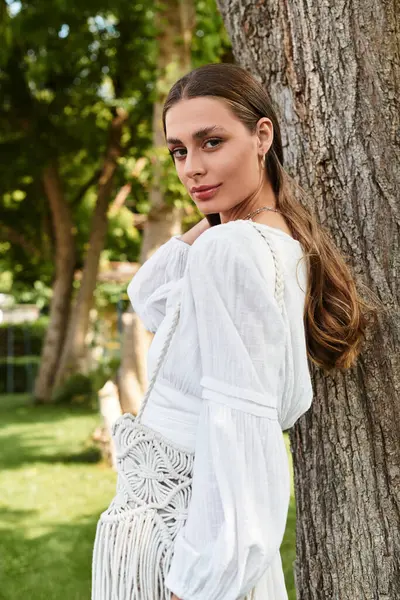 In a sunny garden, a young beautiful woman stands elegantly by a tree, exuding charm and confidence. — Stock Photo