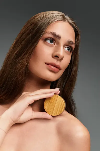 A young beautiful woman poses gracefully with a wooden compact resting gently against her shoulder. — Stock Photo