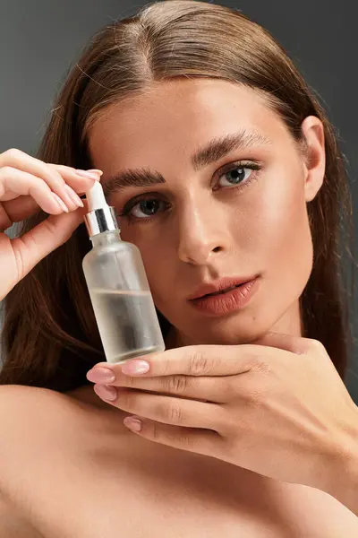 Young beautiful woman showcasing skincare product while highlighting her glowing complexion indoors — Stock Photo