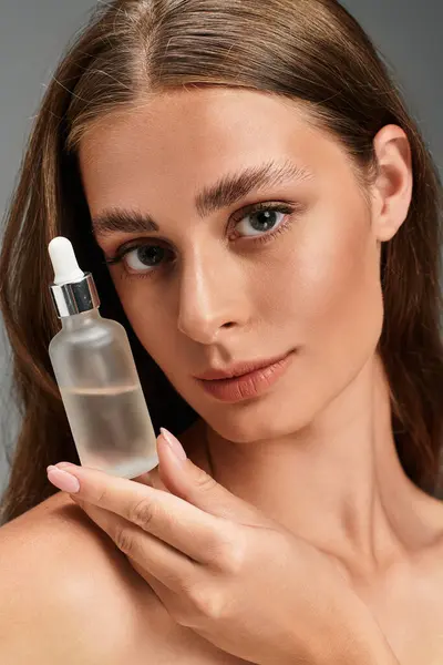 Woman poses confidently while holding a skincare serum, radiating beauty and elegance indoors. — Stock Photo