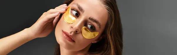 A young woman uses golden eye masks to enhance her skincare for a glowing look. — Stock Photo