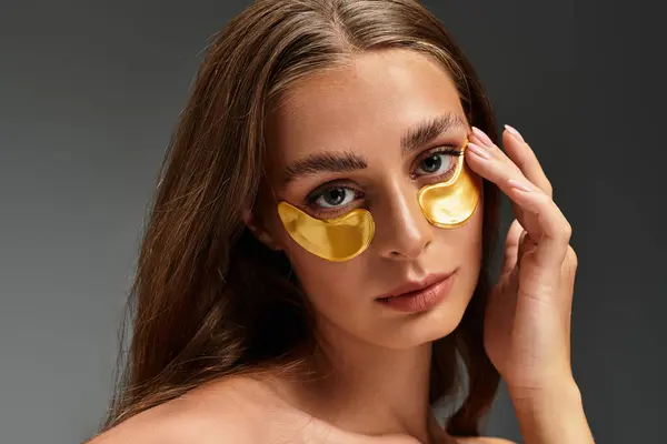 Young woman enhances her natural beauty by applying gold under eye patches for skincare. — Stock Photo