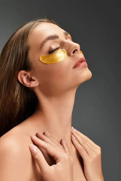 A young beautiful woman relaxes with gold eye masks on her face, enjoying a moment of self care. — Stock Photo