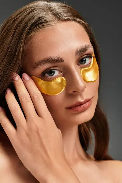 A young beautiful woman enhances her skincare routine with luxurious gold under eye patches. — Stock Photo