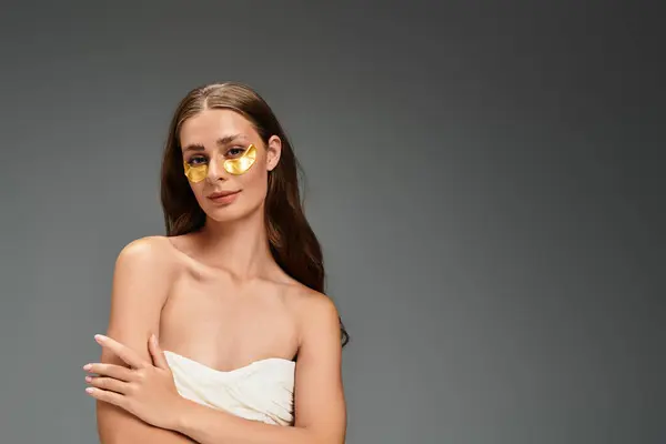 Young woman happily applying golden under eye patches during her self care moment. — Stock Photo