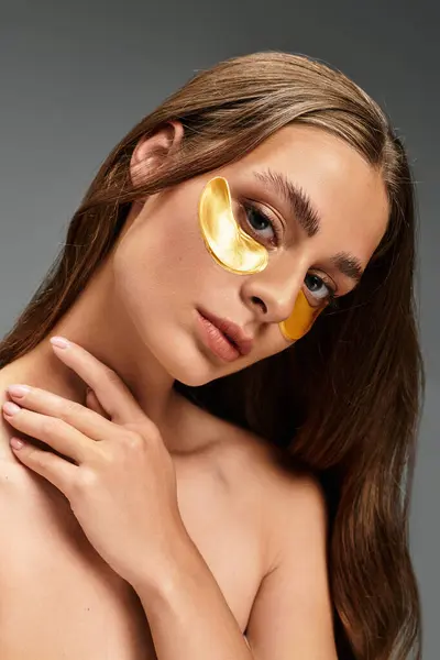 A young woman uses golden eye patches to elevate her serene and elegant skincare routine. — Stock Photo